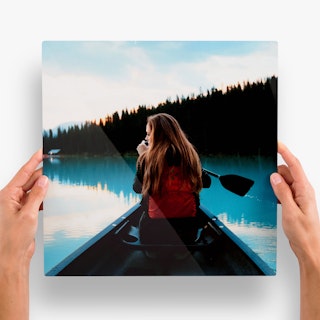 Two hands holding an aluminum print of a woman with a red backpack paddling in a canoe.
