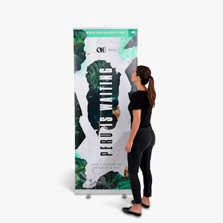 A woman wearing a black outfit standing next to a pop up banner printed with Peru Is Waiting.