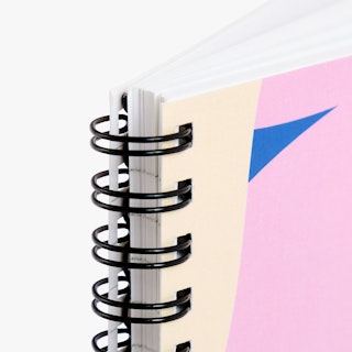 The top corner of a custom notebook printed with a pink, blue and cream cover and bound with black coils.
