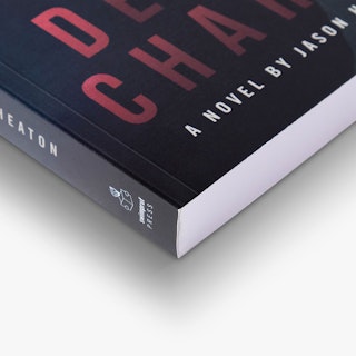 The bottom corner of a paperback book printed with a black cover and letters in red and white.