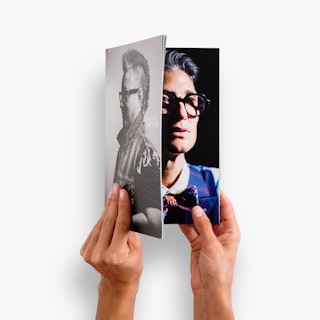 Two hands holding a photography booklet open to an images of a person wearing glasses and a bowtie.
