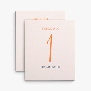 Two wedding place cards overlapping each other with a pink background and peach table numbers.