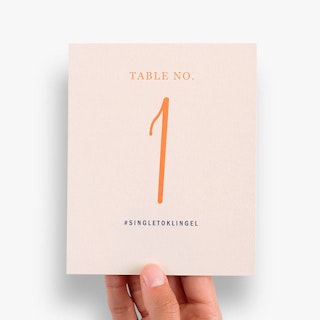 A hand holding a custom place card printed with a pink background and Table No. 1 in orange.