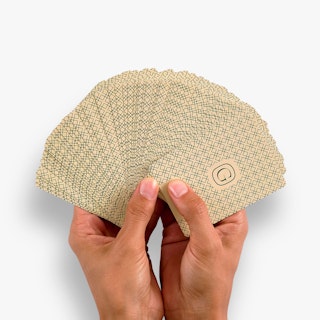 Two hands holding a deck of playing cards fanned out and printed with a green and cream design on the back.