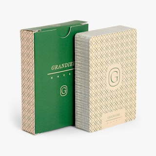 A deck of custom playing cards printed with a green and cream design next to its green box.