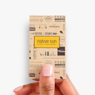 A hand holding a vertical business card printed with native sun in yellow and black with food graphics around it.