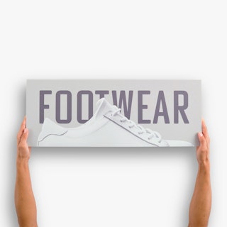 Two hands holding a PVC foam board sign printed with Footwear in dark gray and a white sneaker.