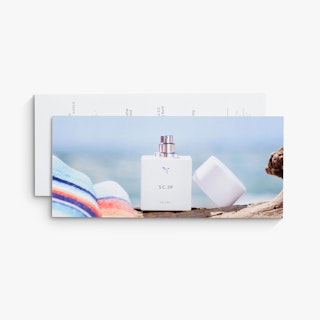 Two business rack cards overlapping each other and printed with a perfume bottle by a beach towel.