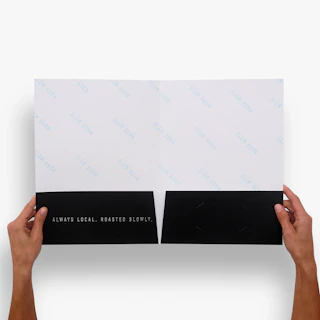 Two hands holding open a custom pocket folder printed with black pockets and silver raised foil.