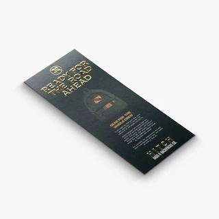 A custom rack card laying down and printed with a dark green background and letters in gold raised foil.