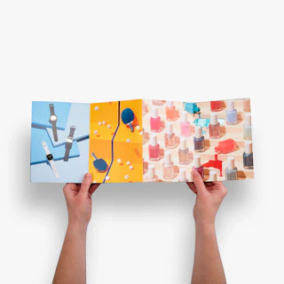 Two hands holding open an accordion fold brochure printed with images of watch, ping pong balls and more.