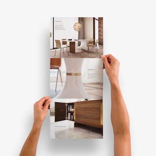 Two hands holding open a vertical tri fold brochure printed with images of modern interior design.