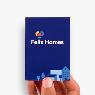 A hand holding a real estate business card printed with a dark blue background, Felix Homes in white and house illustrations.