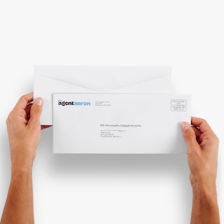 Two hands holding two real estate business envelopes printed with Agent Aaron in dark and light blue.
