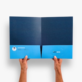Two hands holding a pocket folder open to a dark and light blue interior and real estate agent info.