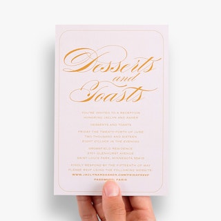 A hand holding a custom reception card printed with Desserts and Toasts and venue details in orange.