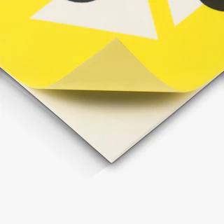 The bottom corner of a custom sticker printed with a yellow design peeling off its backing.