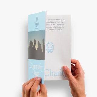 Two hands opening a religious booklet printed with Infinite Love and Community Update on the front.