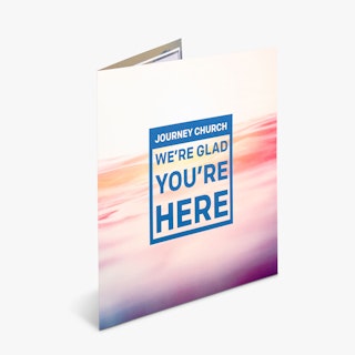 A church brochure standing open and printed with Journey Church We're Glad You're Here on the front.