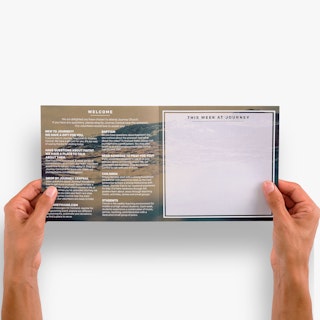 Two hands holding open a church brochure printed with welcome messaging and details.