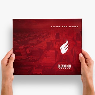 Two hands holding a religious bulletin printed with Taking You Higher Elevation Church in red and white.