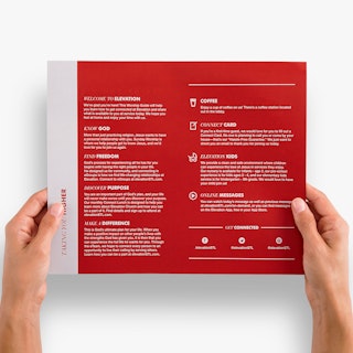 Two hands holding a church bulletin printed with a red background and worship details in white.