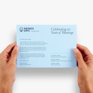 Two hands holding a religious direct mail postcard printed with Infinite Love Worship Center in blue.