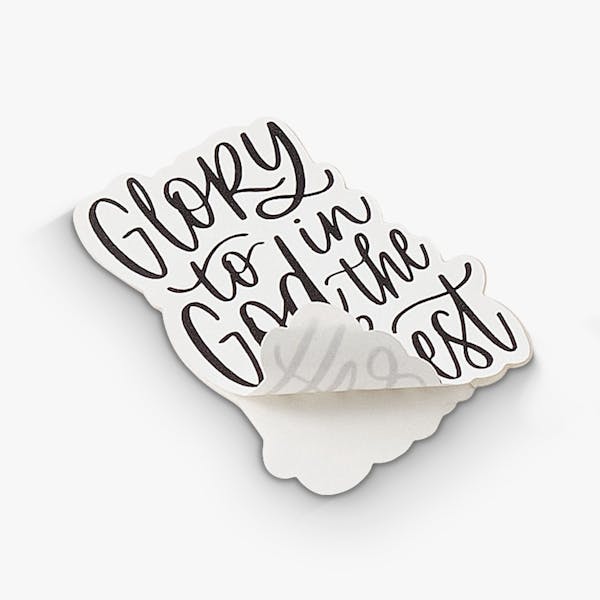 A custom sticker with the bottom corner peeling off the backing and printed with Glory to God in the Highest.