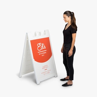A woman wearing a black outfit standing next to a white sidewalk sign printed with Ed's Kitchen SLP.