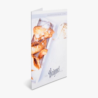 A restaurant brochure standing open and printed with beignets dusted with powdered sugar on the front.