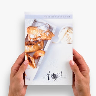 Two hands holding a custom brochure printed with The Beignet Bar and an image of beignets.