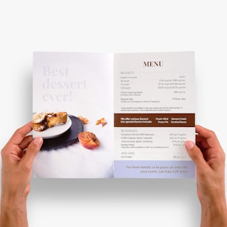 Two hands holding open a restaurant brochure printed with menu items inside.