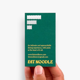 A hand holding a custom business card printed with three die cuts, a green background and yellow text.