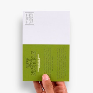 A hand holding a direct mail postcard printed in green and white with information about Fat Noodle restaurant.