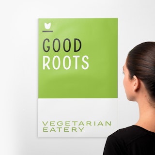 A woman standing in front of a wall decal printed with Good Roots Vegetarian Eatery in green, white and black.