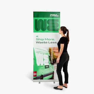 A woman wearing a black shirt and jeans standing next to a retractable banner printed with a green design.