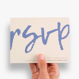 A hand holding an RSVP card printed with rsvp in blue and return details along the bottom in black.