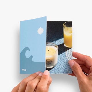 Two hands opening a saddle stitch booklet printed with a blue wave design on the front and an image of candles inside.