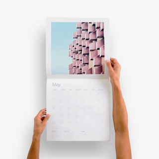 Two hands holding open a wall calendar to May and an image of abstract architecture.