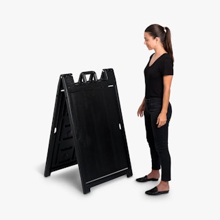 A woman wearing a black outfit standing next to a black sandwich board sign.