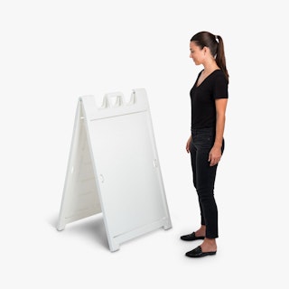 A woman wearing a black outfit standing next to a white A-frame sidewalk sign.