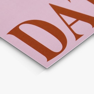 The bottom corner of a save the date card printed with a pink background and red capital letters.