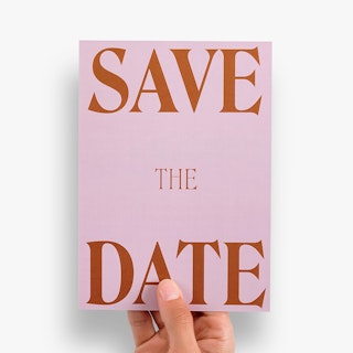 A hand holding a custom save the date card with a pink background and Save The Date in dark orange.