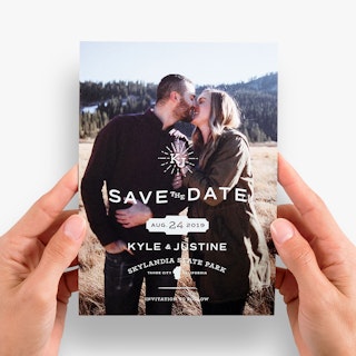 Two hands holding a custom save the date magnet printed with Kyle & Justine and Skylandia State Park.