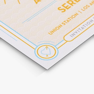 The bottom corner of a save the date postcard printed with a yellow and blue heart with an arrow through it.