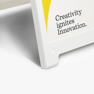 The bottom corner of a white sandwich board sign holding a sign printed in white, black and yellow.