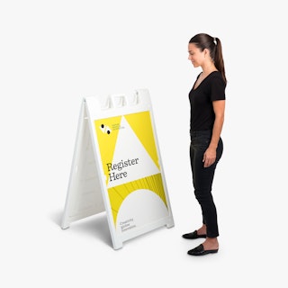 A woman wearing a black outfit standing next to a white A-frame with a yellow and white printed sign.