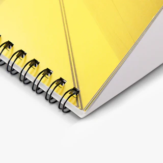 The corner of a desk calendar printed with a yellow and black cover and black wire coils binding it.