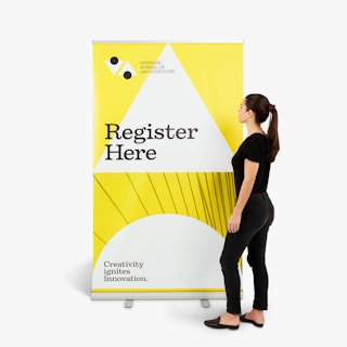 A woman wearing a black shirt and jeans standing next to a school pop up banner in yellow, white and black.