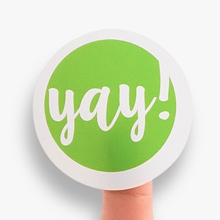 A finger with a custom sticker stuck to it that's printed with Yay in white and bright green.